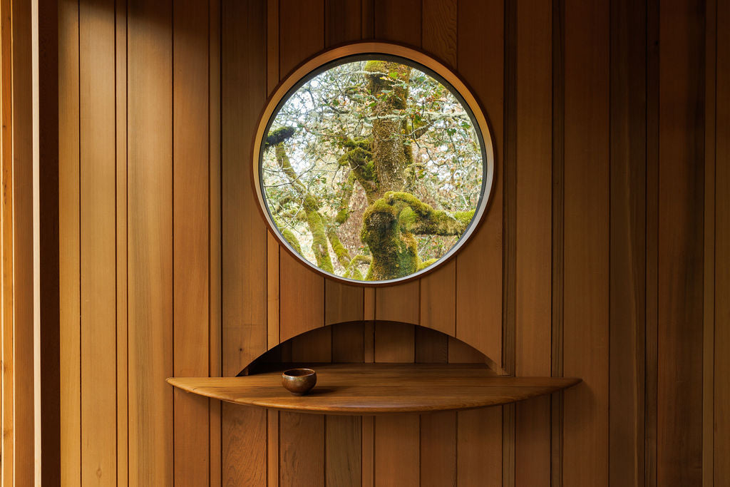 A wooden half circle built-in shelf sits below a circular portal window. The shelf matches the wood paneling on the walls with a warm chestnut brown colour.