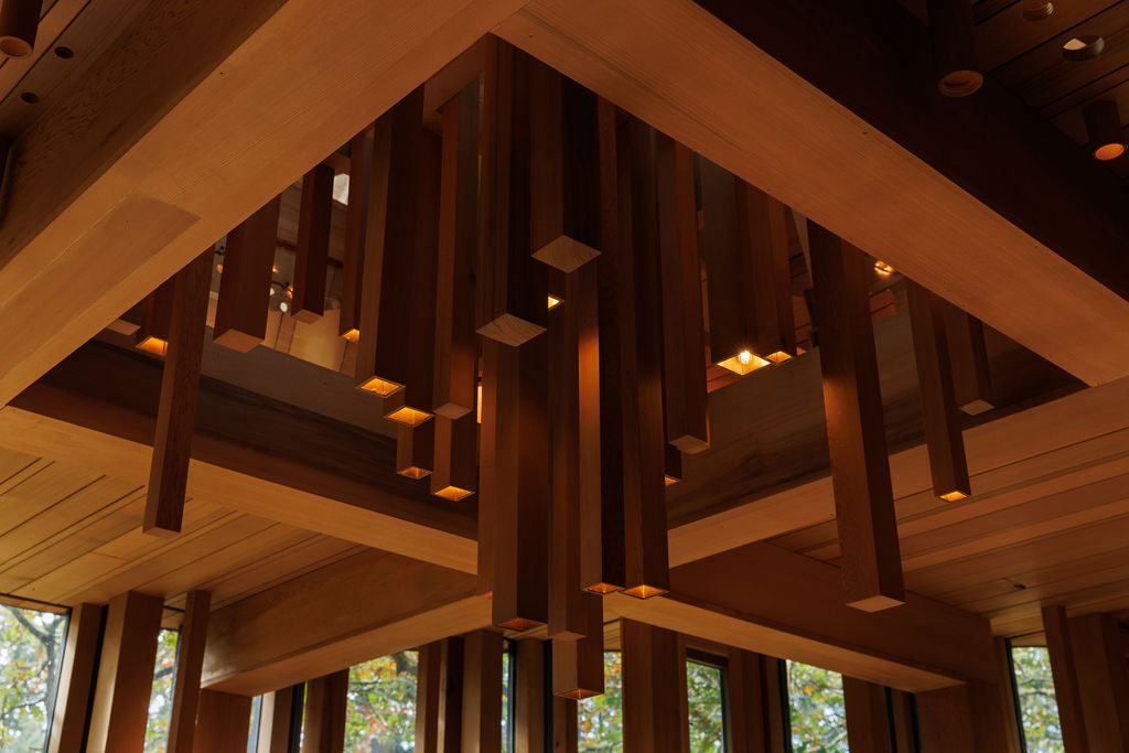 A geometric light fixture custom made with a warm chestnut brown colour. It has different lengths of rectangular wood placed vertically while the light comes out of the end of each rectangular piece.