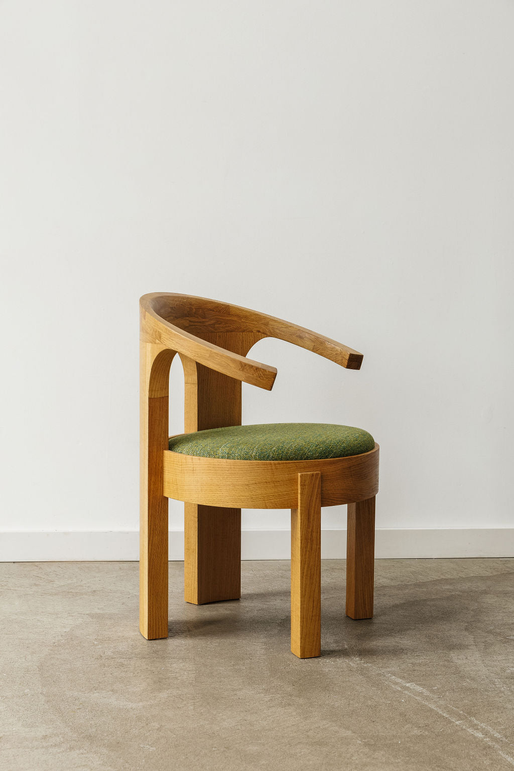 A custom made wood dining chair reminiscent of mid-century modern design. The back of the chair is curved and the seat is a perfect circle and has light green upholstery.