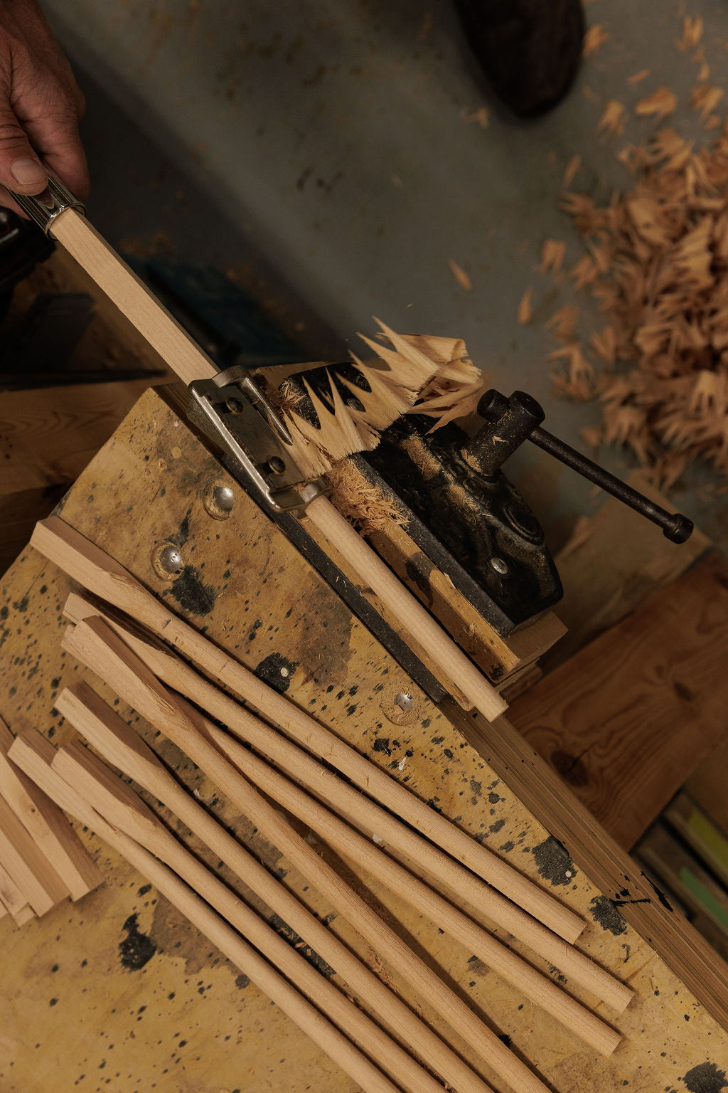 A birds eye view of wooden dowels being carved. With wood shavings falling to the floor.