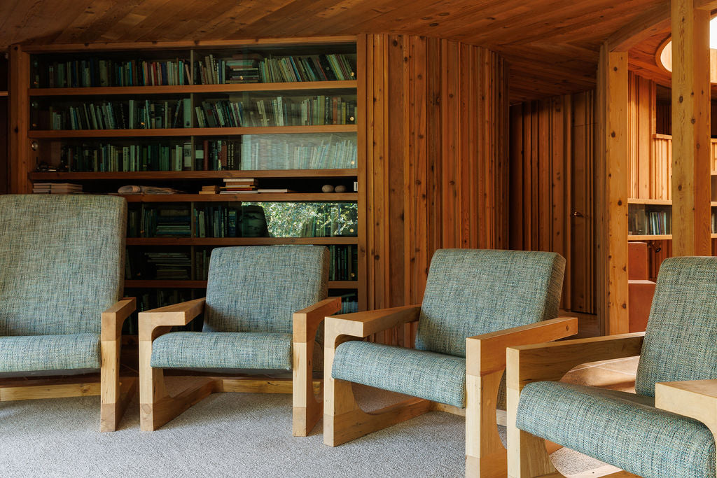 Four handmade wooden chairs with green textured upholstery in a wood-panelled room. The chairs have a geometric frame.