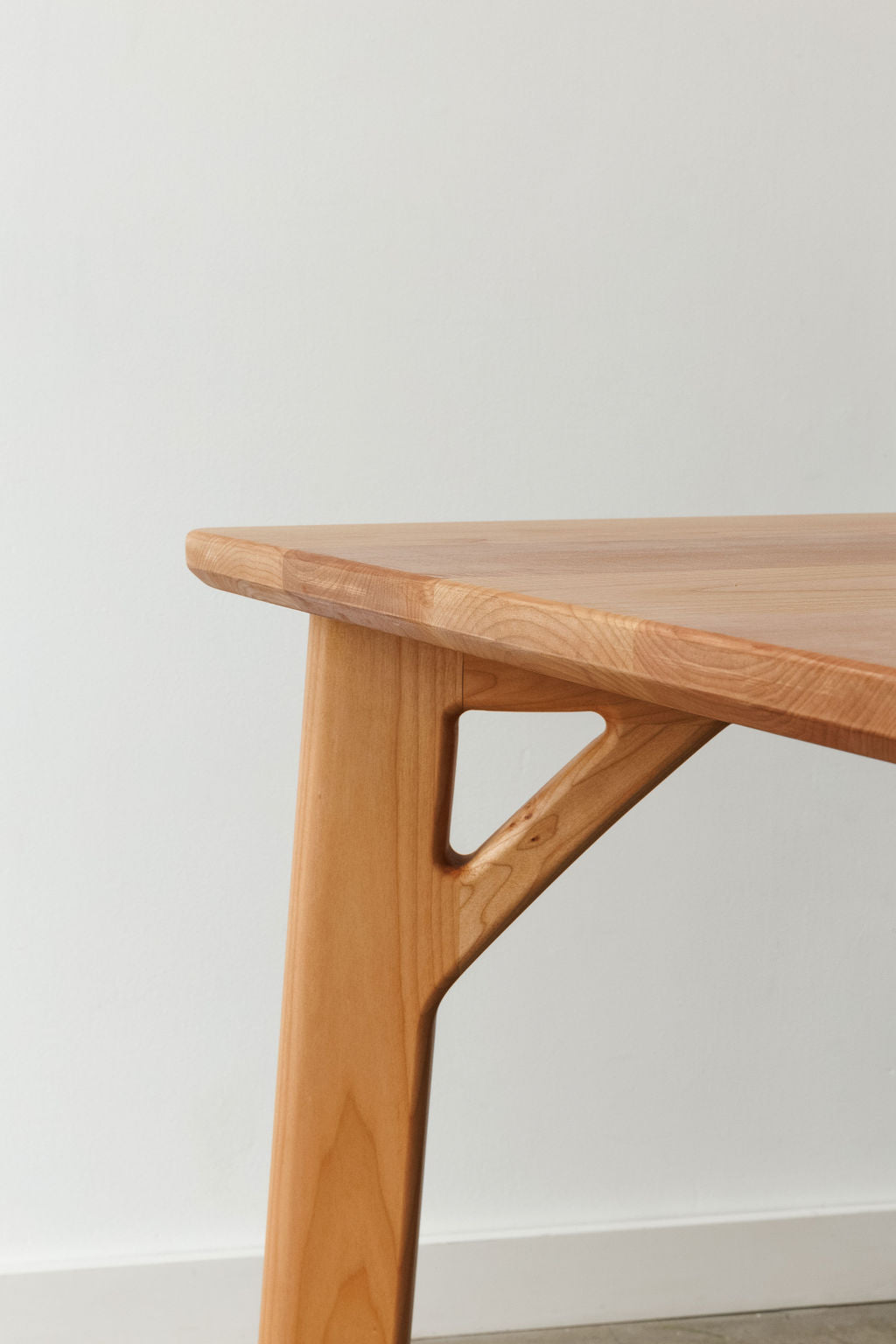 Close up of the corner of a handmade, modern minimal table in a light wood material.