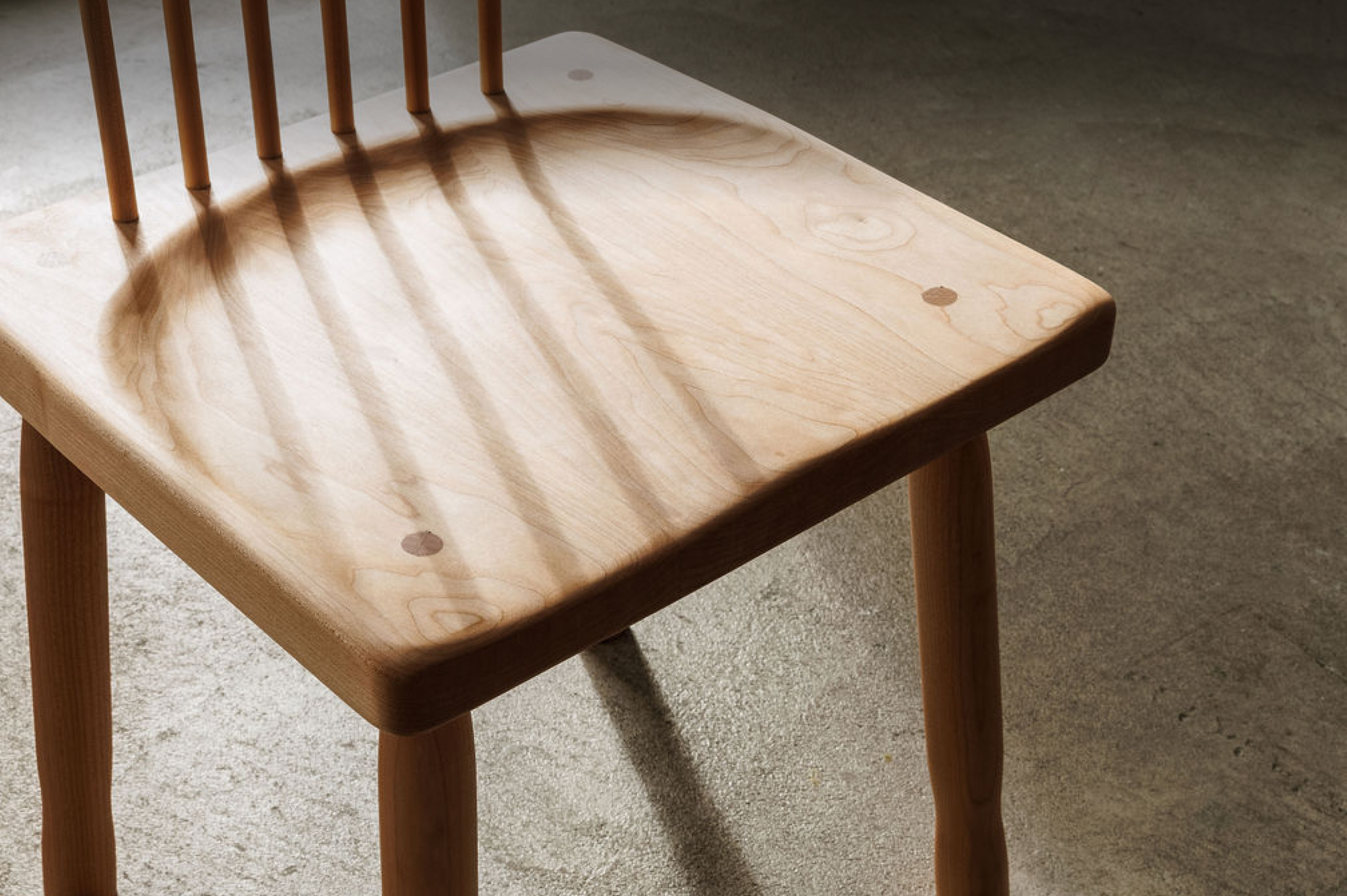 The seat of a wooden dining chair is shown with light coming through the back of the chair and creating a shadow.