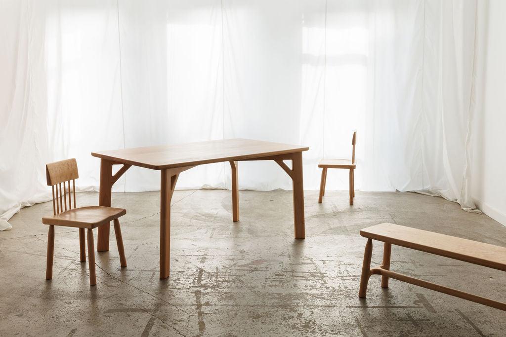  A minimalist wooden table with two chairs and a bench placed in an bright empty room, creating a minimalistic and inviting atmosphere.