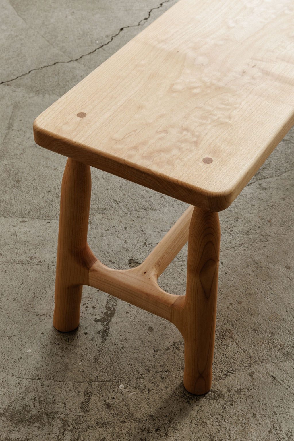 A light colored wooden bench on a concrete floor, providing a comfortable seating option in a simple and sturdy design.